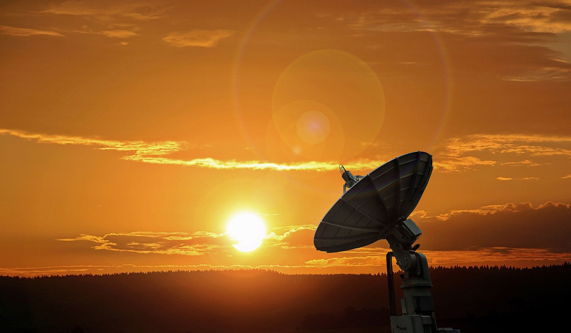 Uma imagem de uma estação terrestre de satélite AWS com o Sol se aproximando do horizonte ao fundo