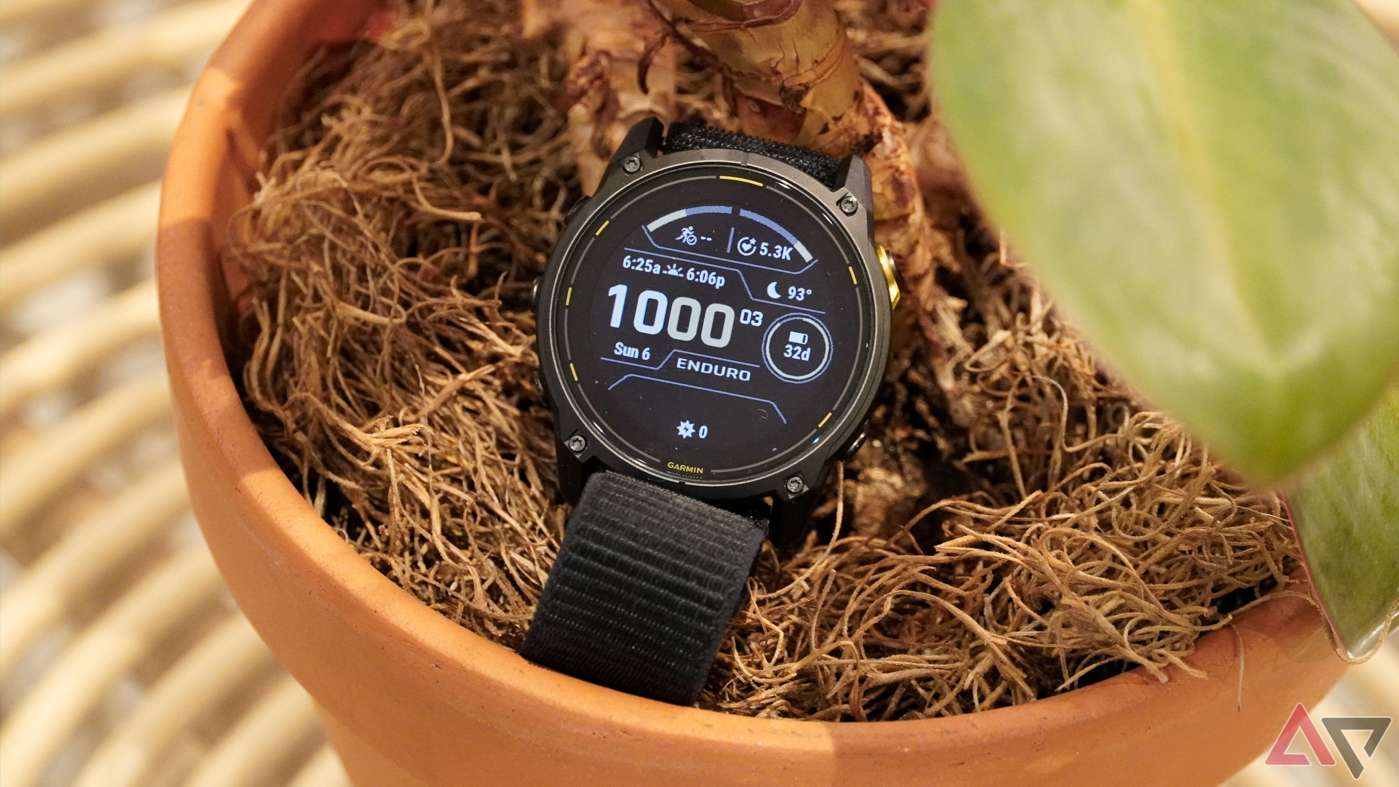 O relógio Garmin Enduro 3 em um vaso de planta com luz de fundo ligada.