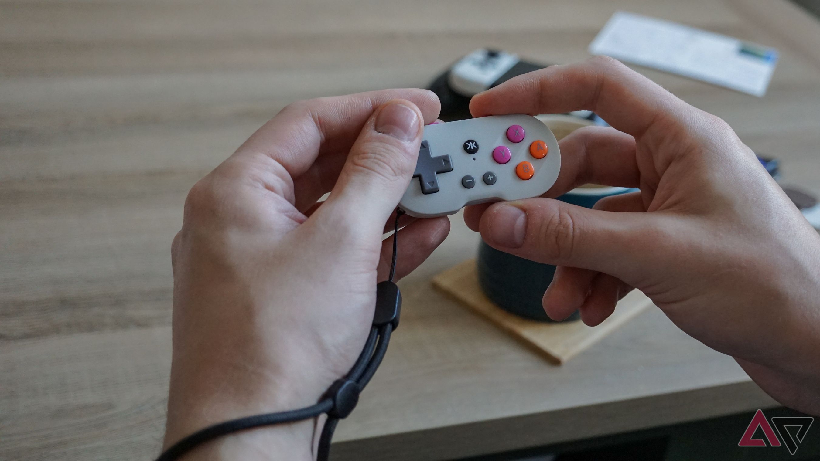 mãos segurando um pequeno controlador Atom cinza com pulseira