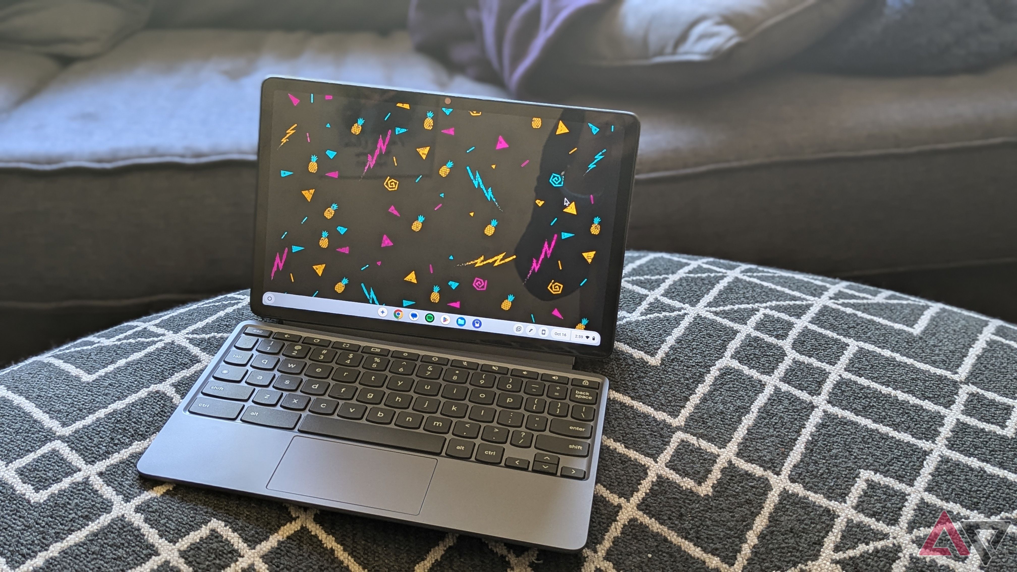 Um Lenovo Chromebook Duet 11 (2024) com fundo de abacaxi sentado em uma poltrona preta com padrão branco em frente a um sofá azul