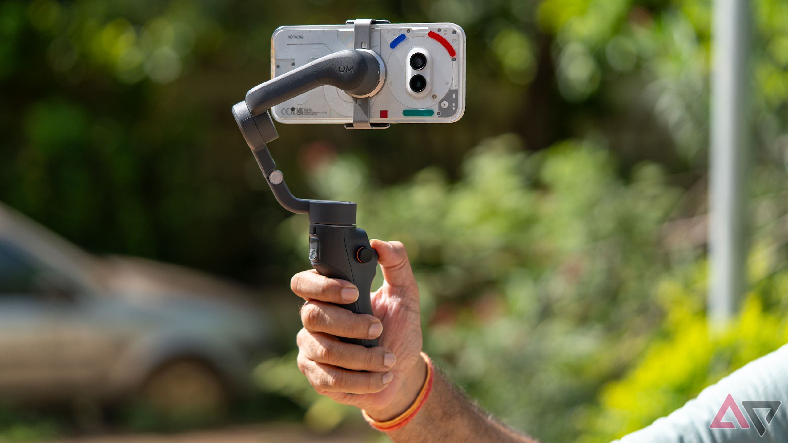 gimbal voltado para a câmera com a mão do operador visível contra um fundo verde exuberante