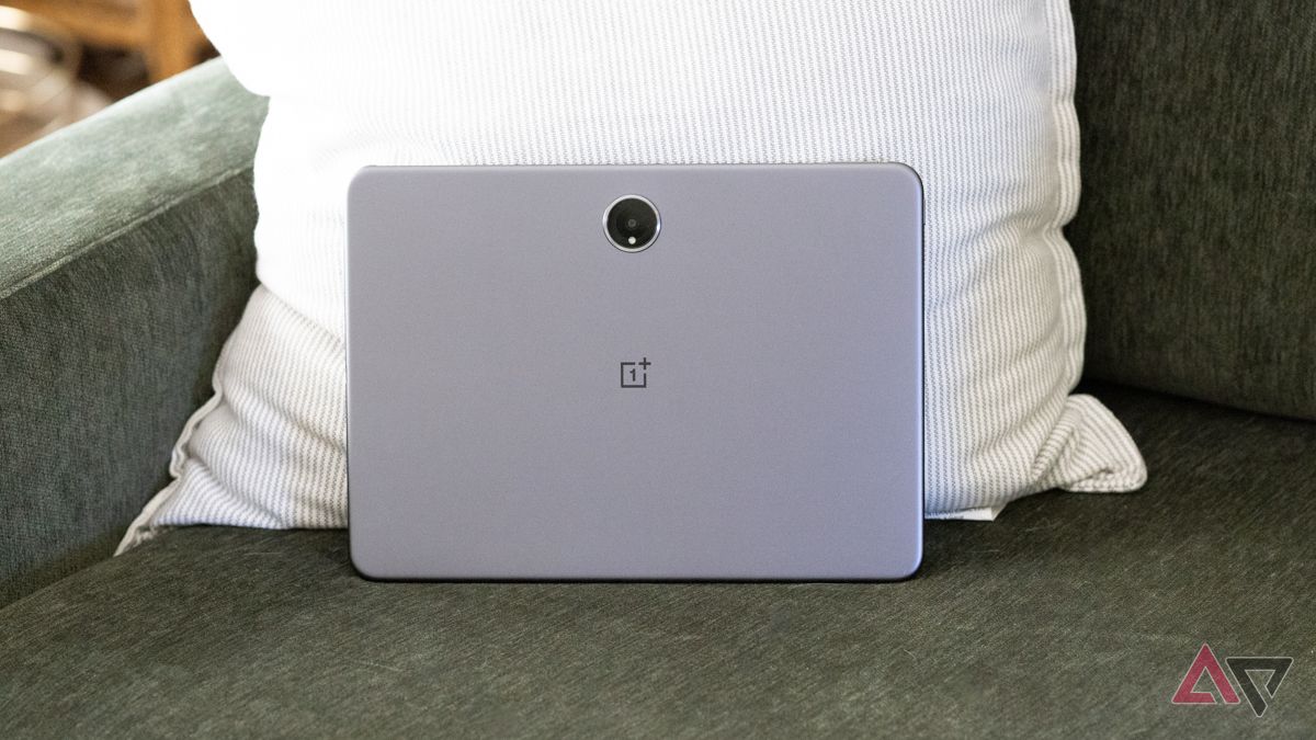 A parte de trás de um OnePlus Pad 2 apoiado em um sofá verde e travesseiro listrado