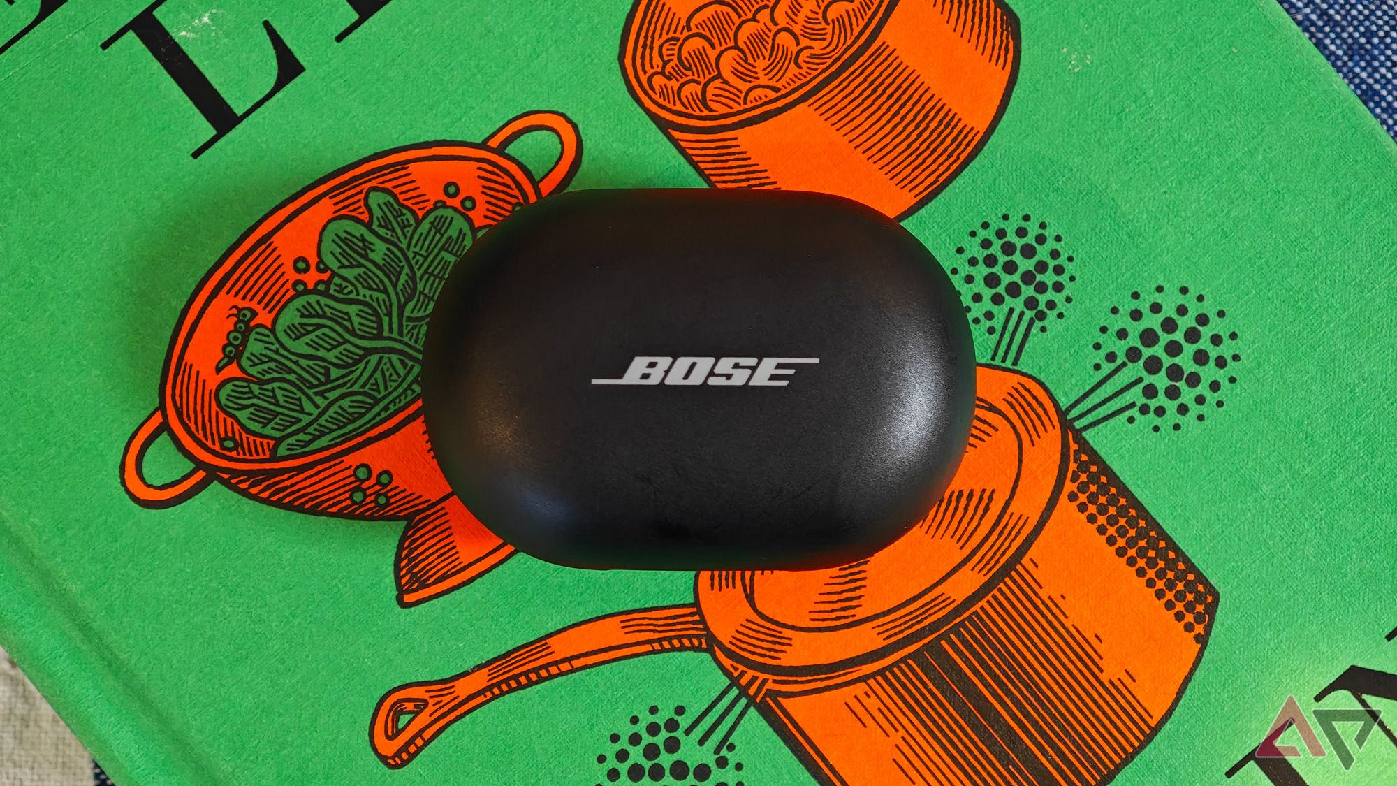 Estojo Bose QuietComfort Earbuds apoiado em um livro de receitas verde