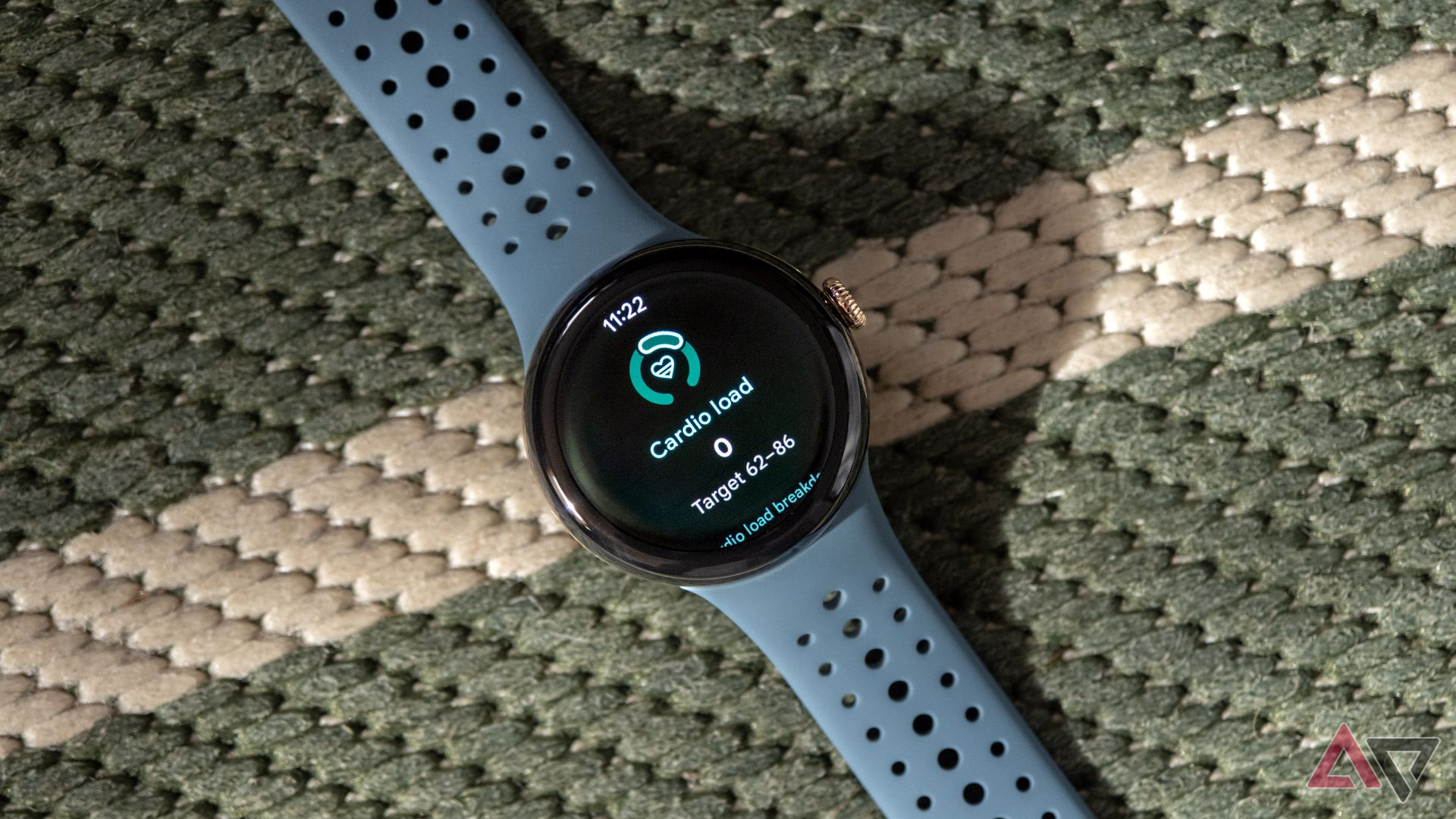 O Google Pixel Watch 3 fica em uma superfície tecida verde e branca com o recurso Cardio Load na tela. 