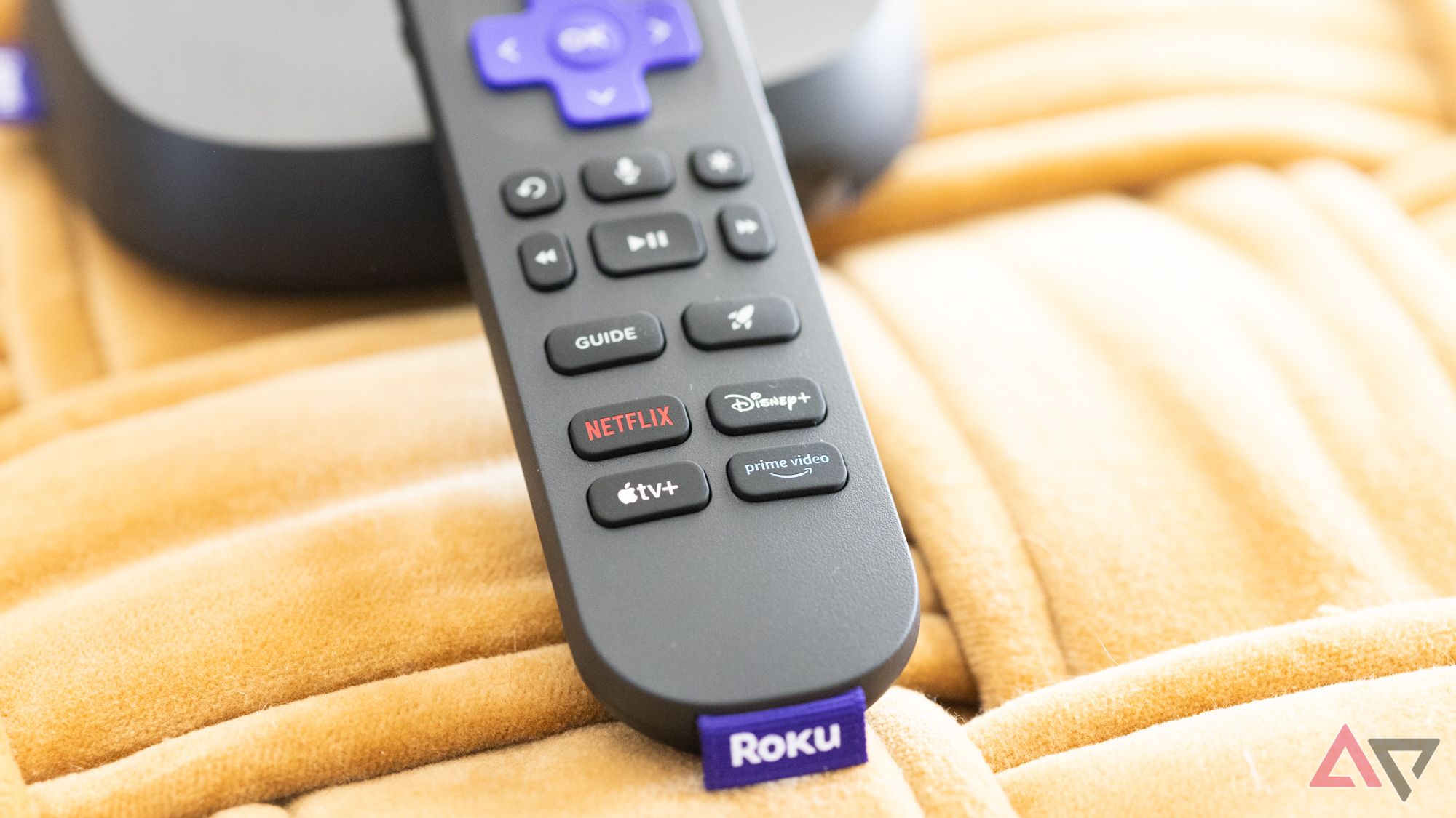 O Roku Ultra Voice Remote Pro mostrando os botões dedicados em um fundo amarelo