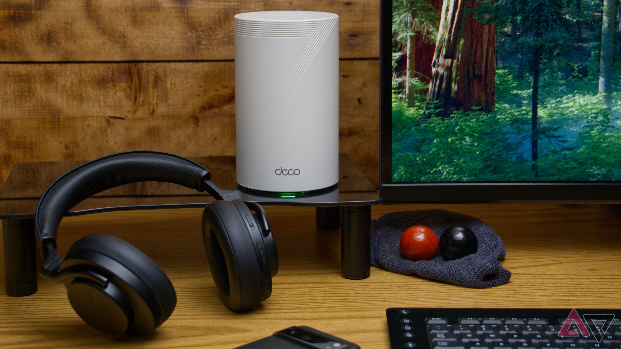 TP-Link Deco BE65 Pro sentado em um suporte de mesa ao lado de vários outros itens com fundo de madeira