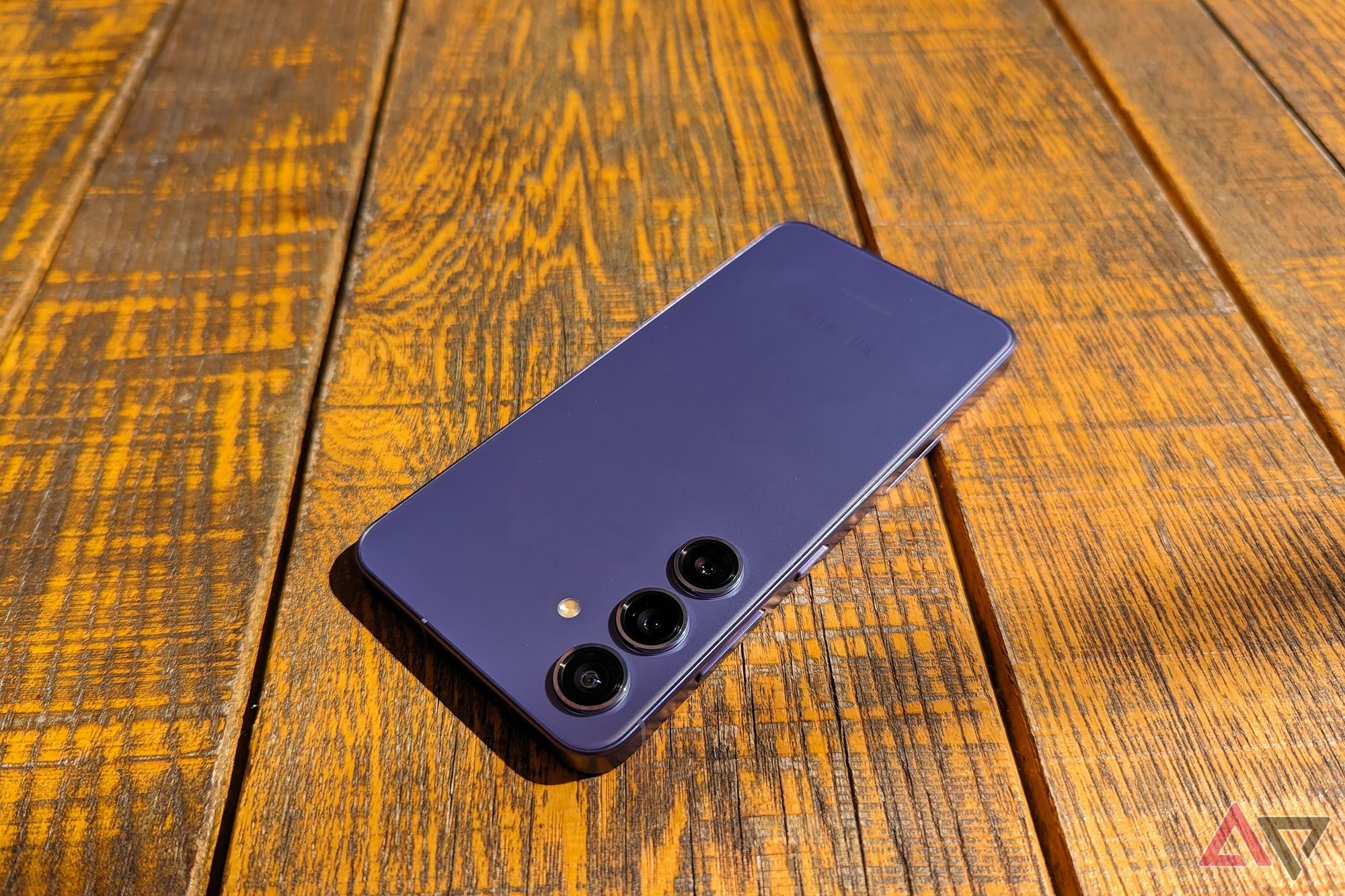 O Samsung Galaxy S24 de cabeça para baixo em uma ensolarada mesa de madeira em Cobalt Violet