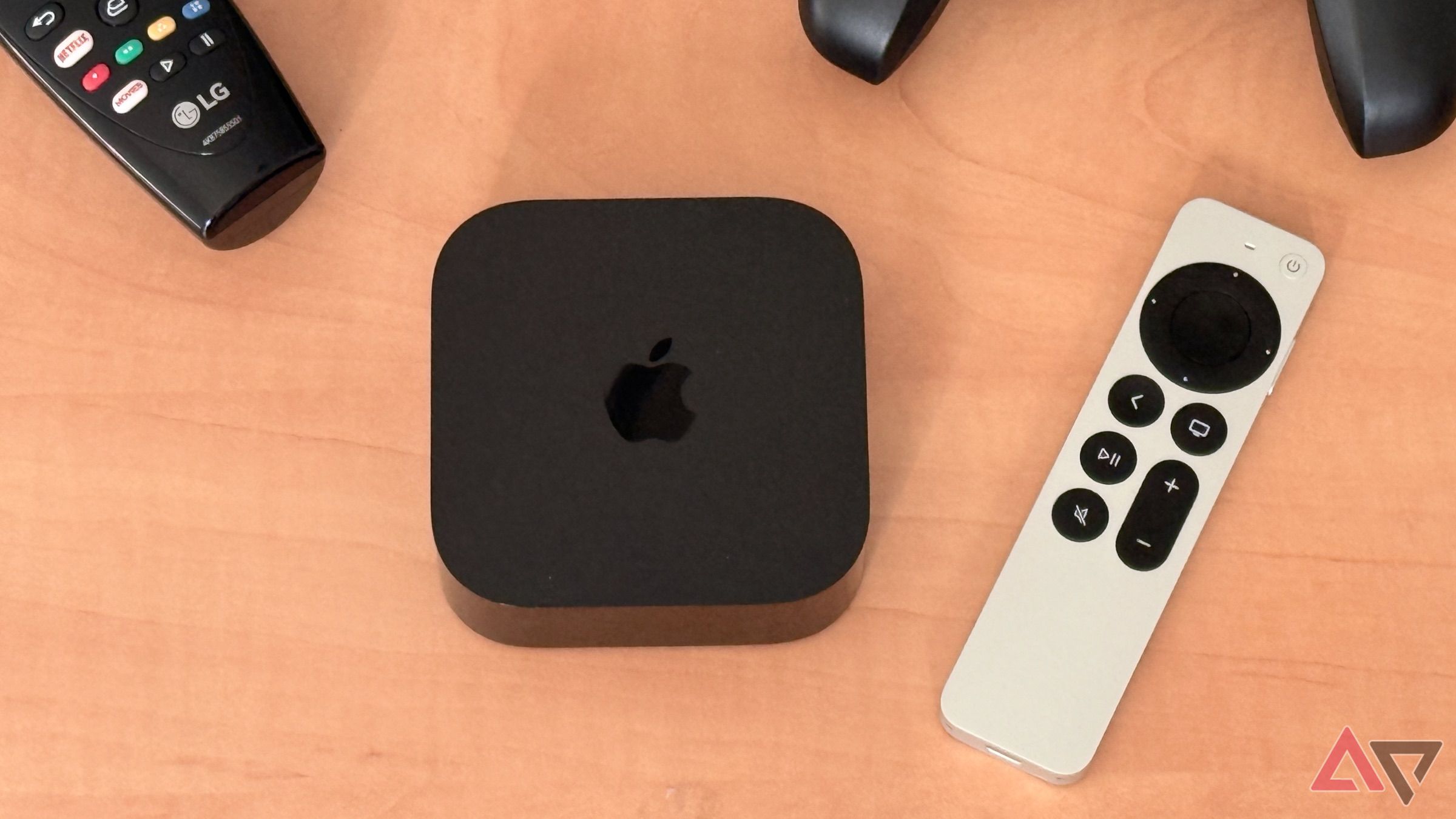 Apple TV 4K em mesa de madeira clara com Siri Remote, LG TV Remote e Nimbus Game Controller