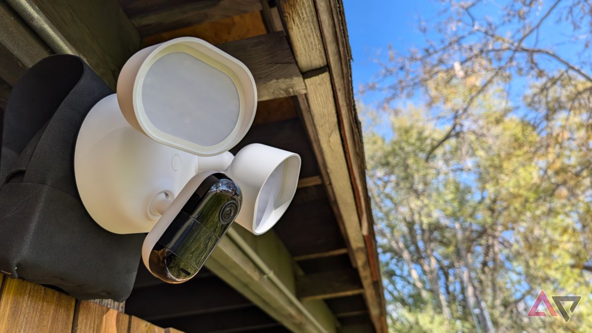 Arlo Wired Floodlight Camera sob uma saliência com cerca e árvore ao fundo