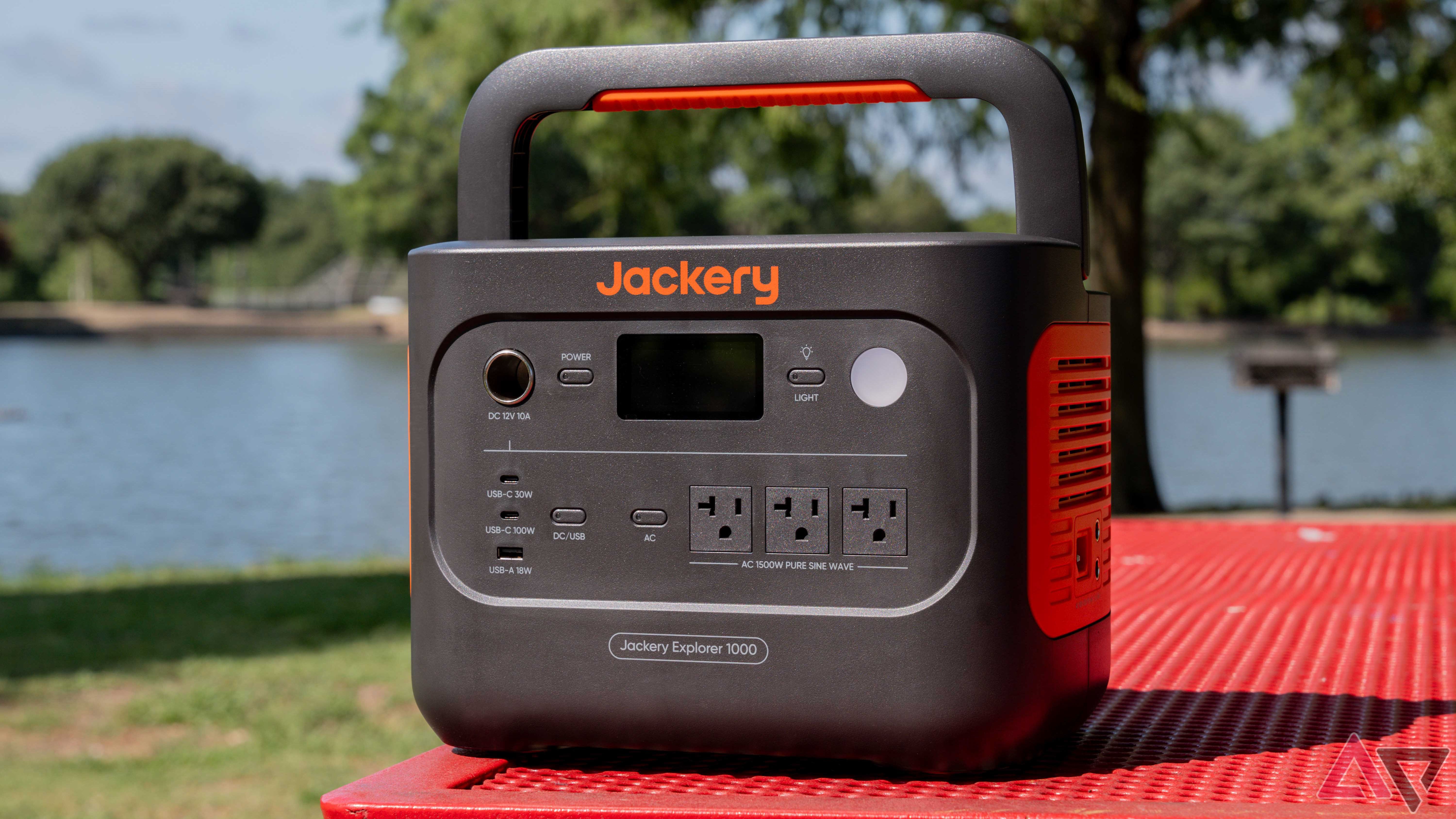 O Jackery Explorer 1000 v2 em um banco de parque vermelho com um lago ao fundo