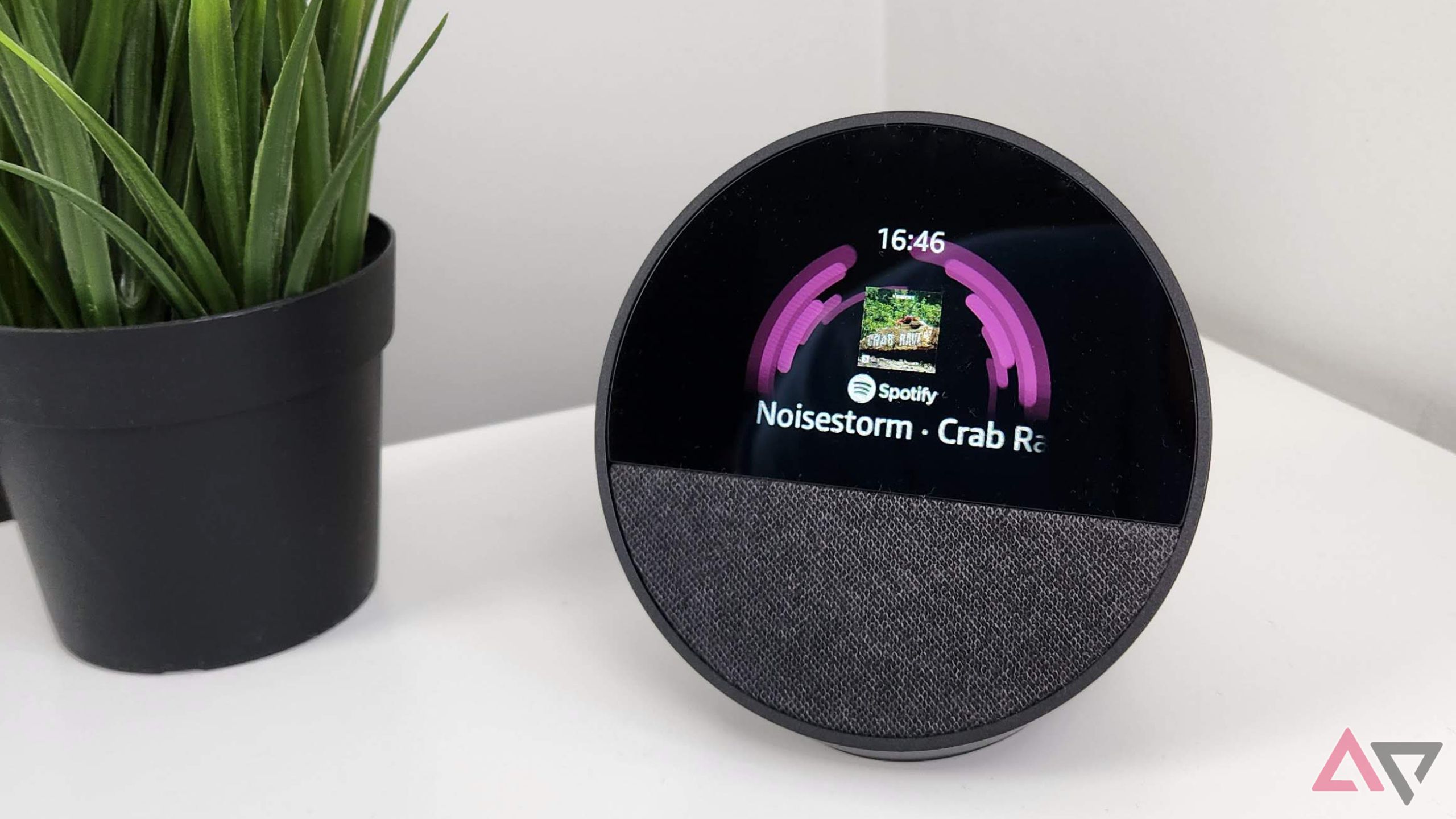 Amazon Echo Spot em uma mesa branca ao lado de uma planta verde mostrando a tela de reprodução de áudio