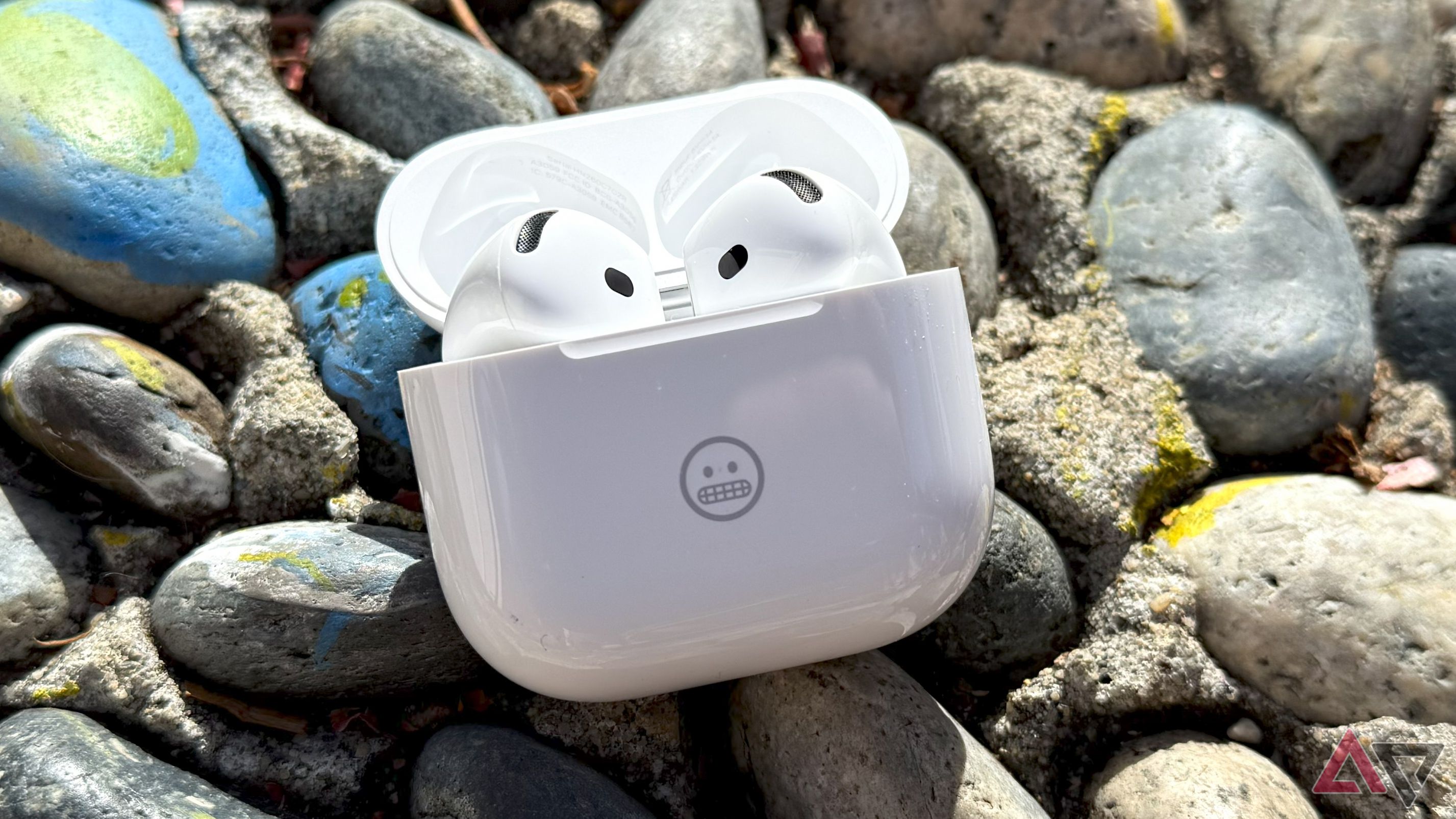 Fones de ouvido AirPods 4 em seu estojo de carregamento sobre pedras