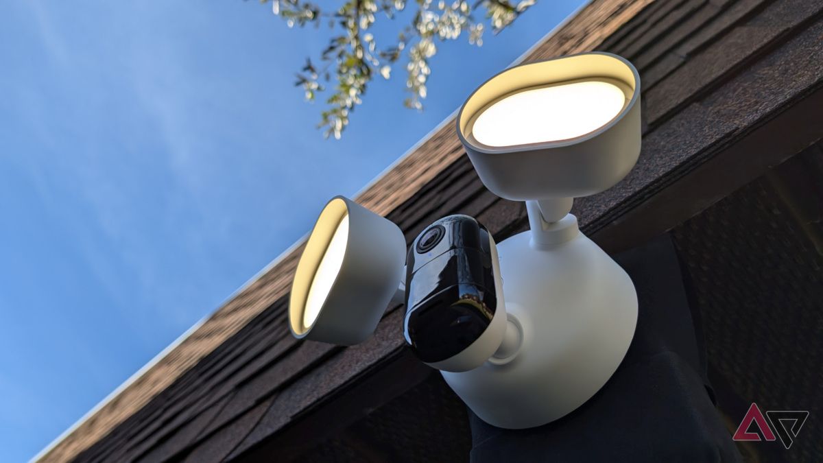 Arlo Wired Floodlight Camera sob saliência com telhado e árvore no fundo com luzes acesas