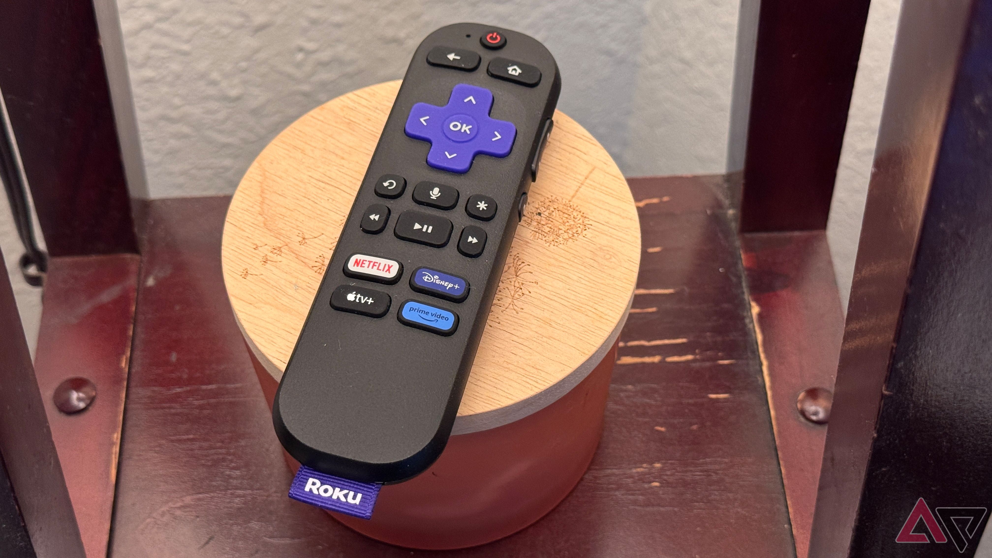 Roku Streaming Stick 4K Remote em um frasco de vela com uma tampa de madeira clara que está apoiada em uma prateleira de madeira.