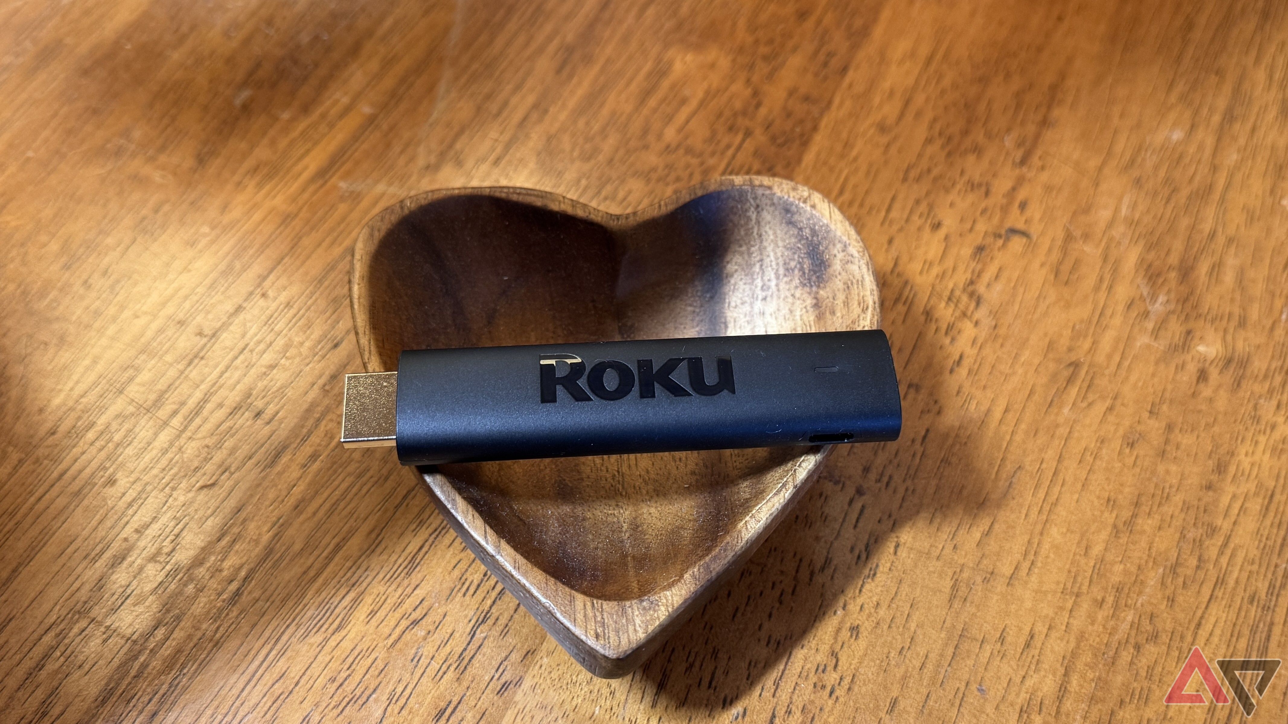 Roku Streaming Stick 4K apoiado horizontalmente em uma tigela de madeira em forma de coração.