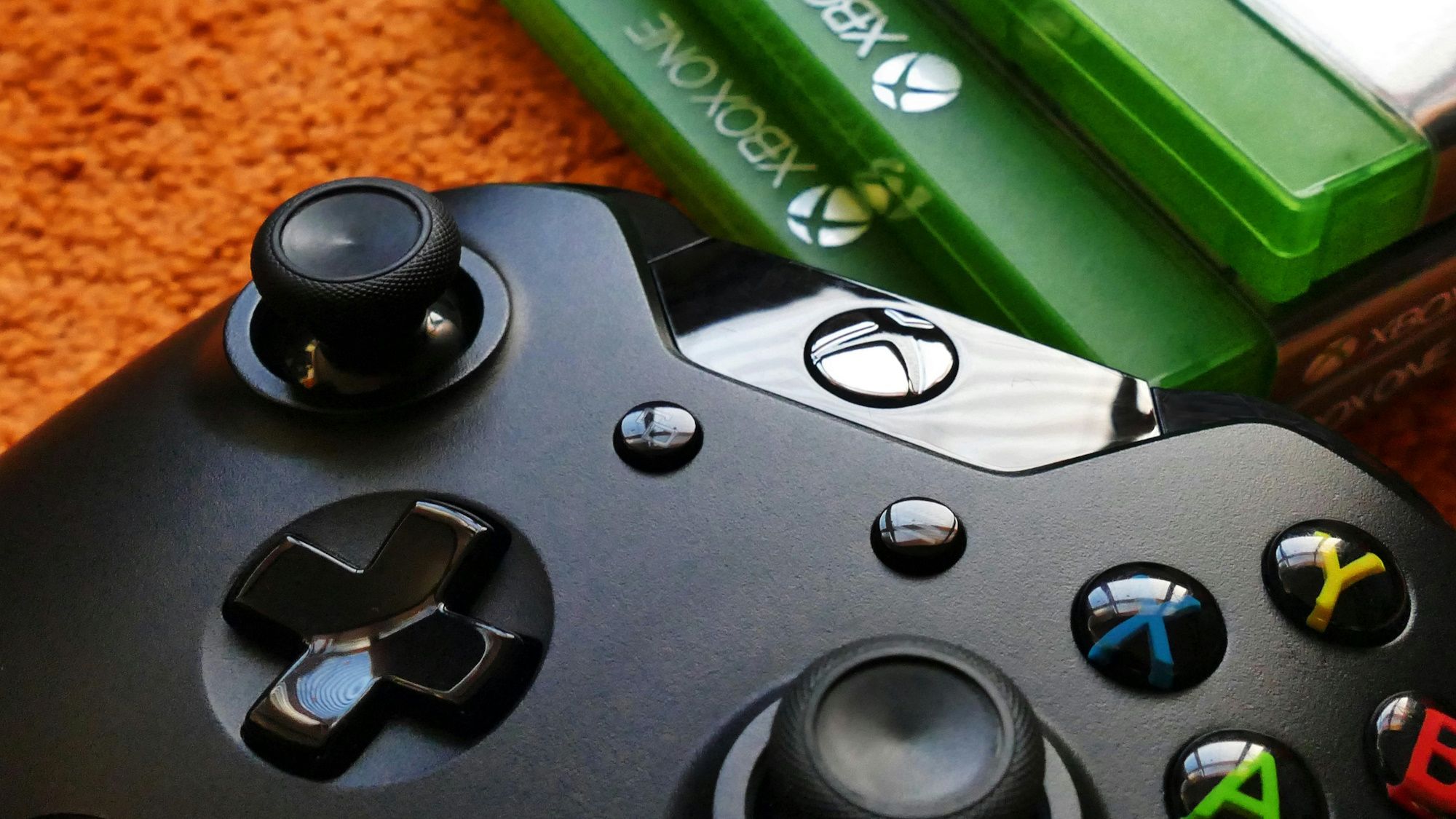 Close de um controle de xbox preto ao lado de uma pilha de jogos do Xbox One