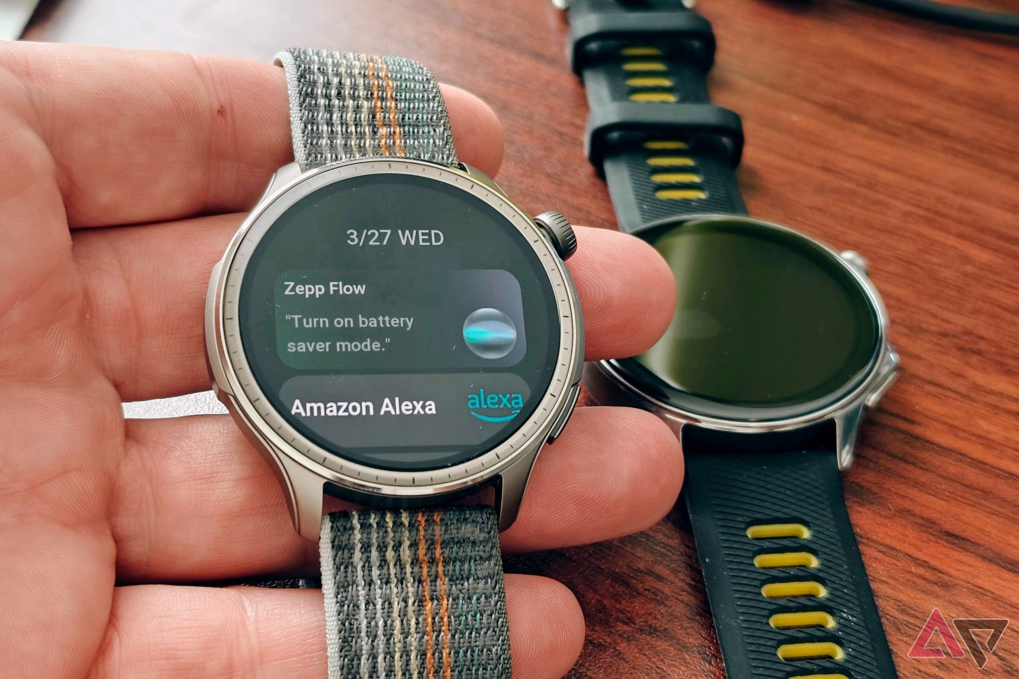 Amazfit Balance na mão mostrando assistentes de voz com OnePlus Watch 2 em uma mesa