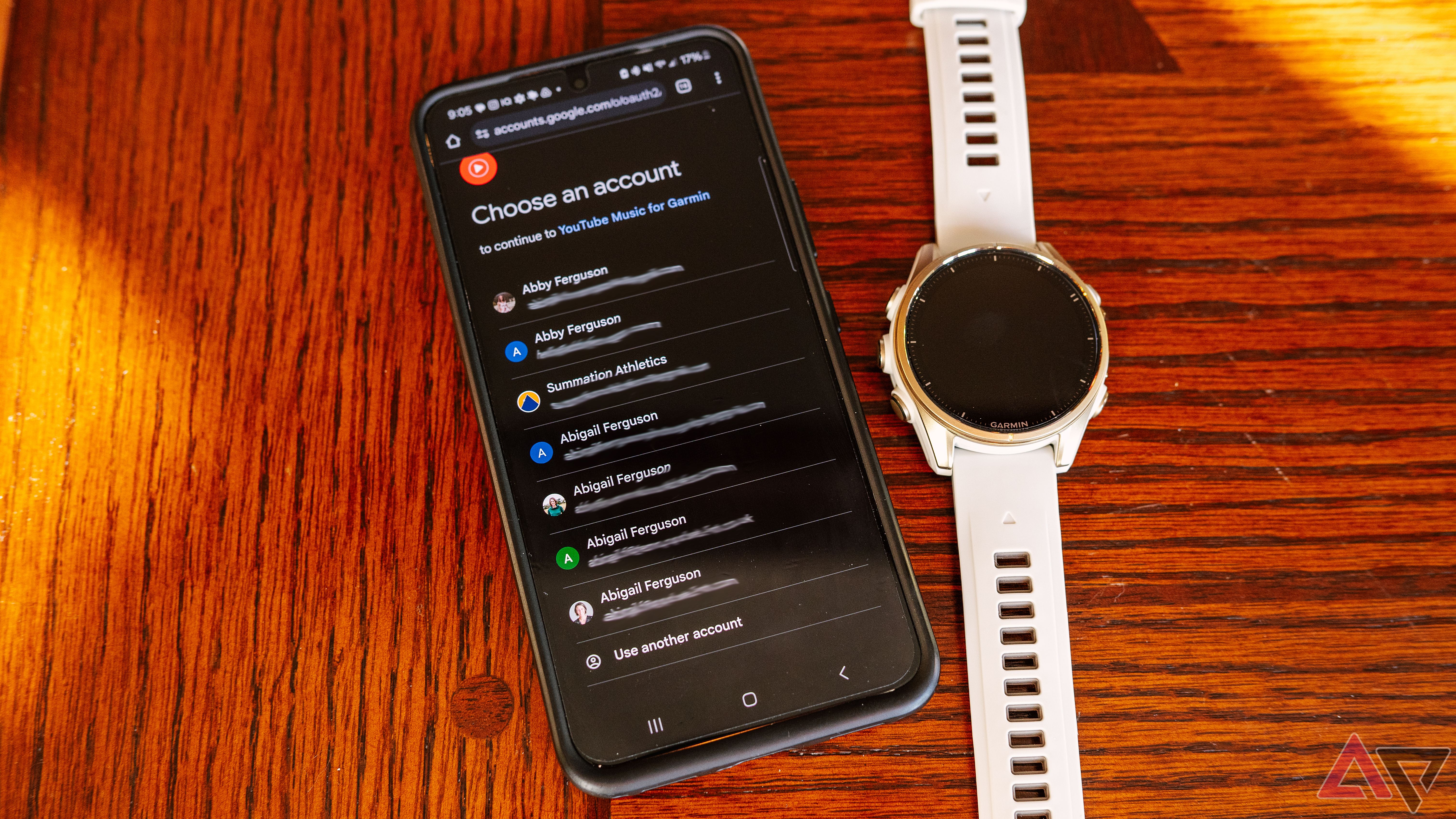 Um telefone Samsung Galaxy com contas do Google na tela fica ao lado de um relógio Garmin fenix 8. 