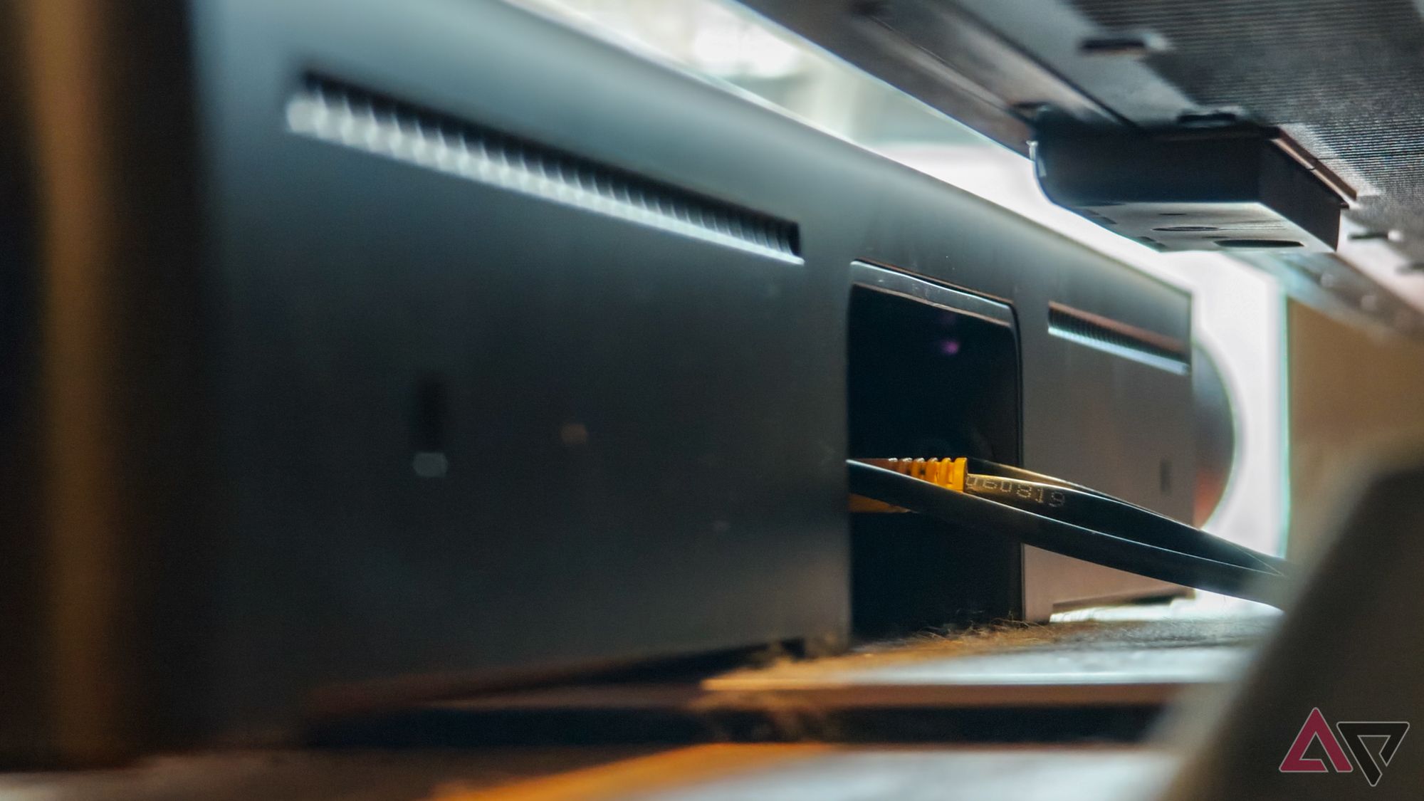 Barra de som Sonos Arc Ultra preta apoiada em um gabinete de madeira de teca, fotografada por trás e abaixo da TV para mostrar os cabos conectados