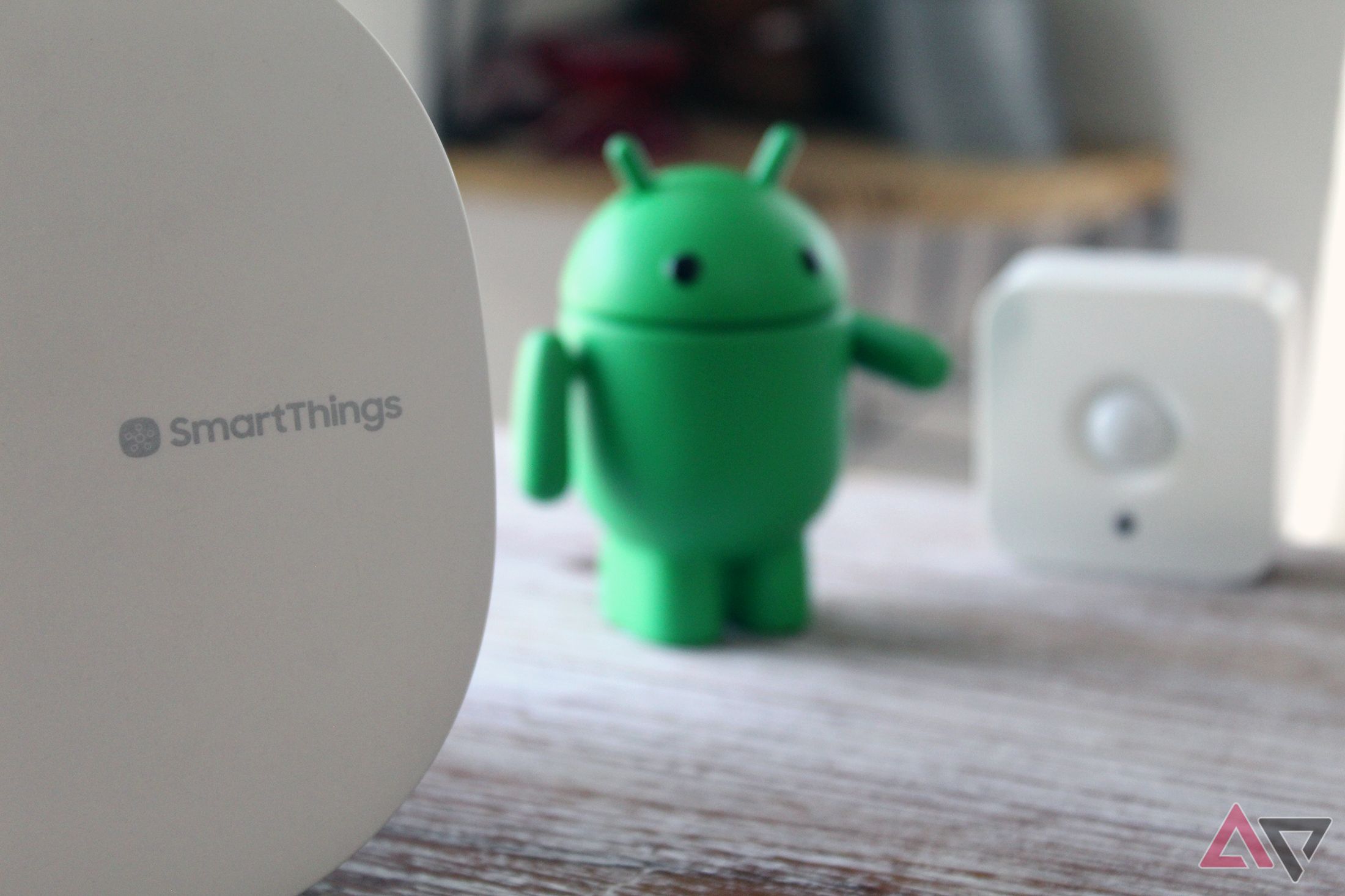 Foto de um hub Samsung SmartThings próximo a um sensor de movimento Philips Hue com uma estatueta Android entre os dois.