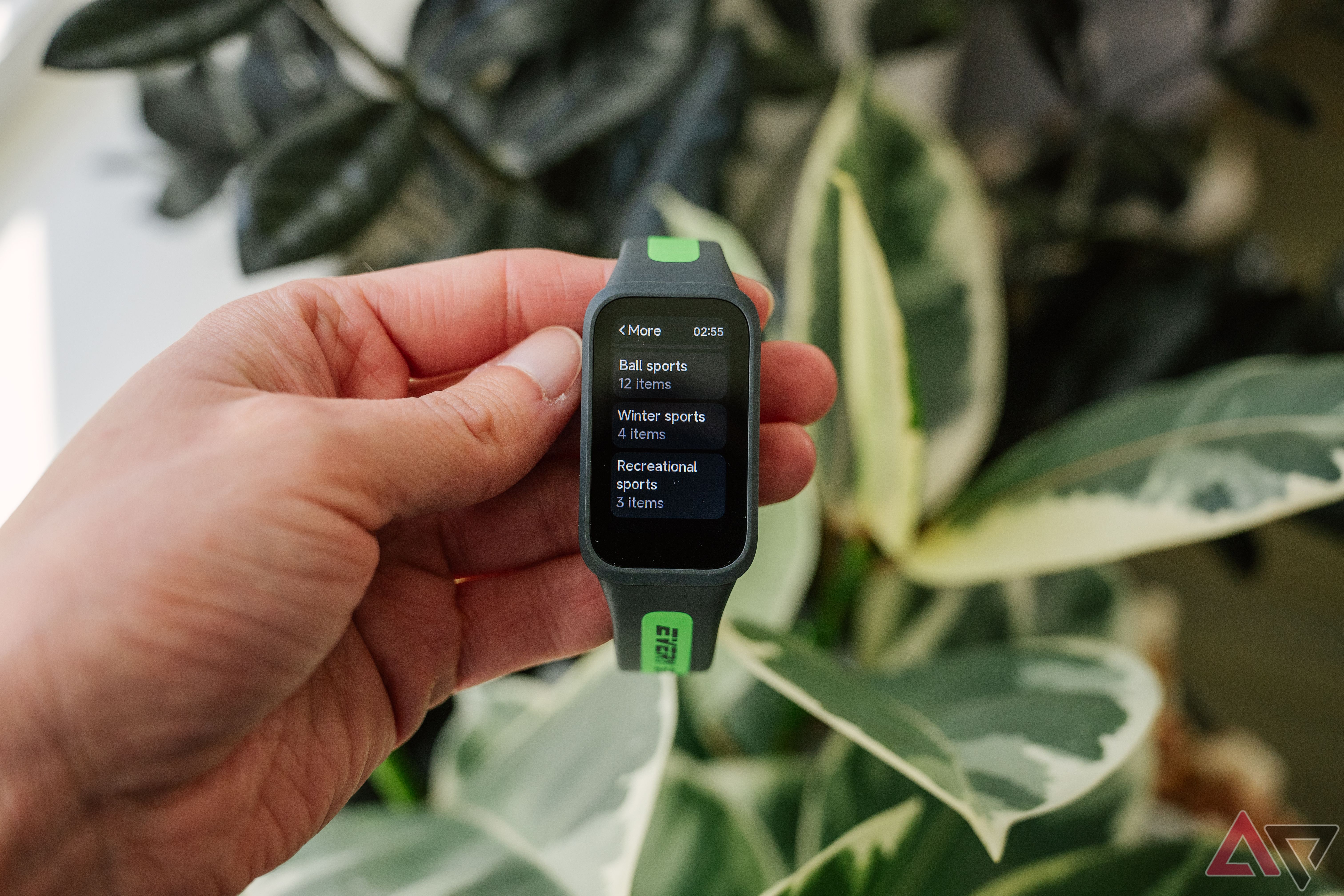 Uma mão segura a Xiaomi Smart Band 9 Active acima de plantas verdes desfocadas.