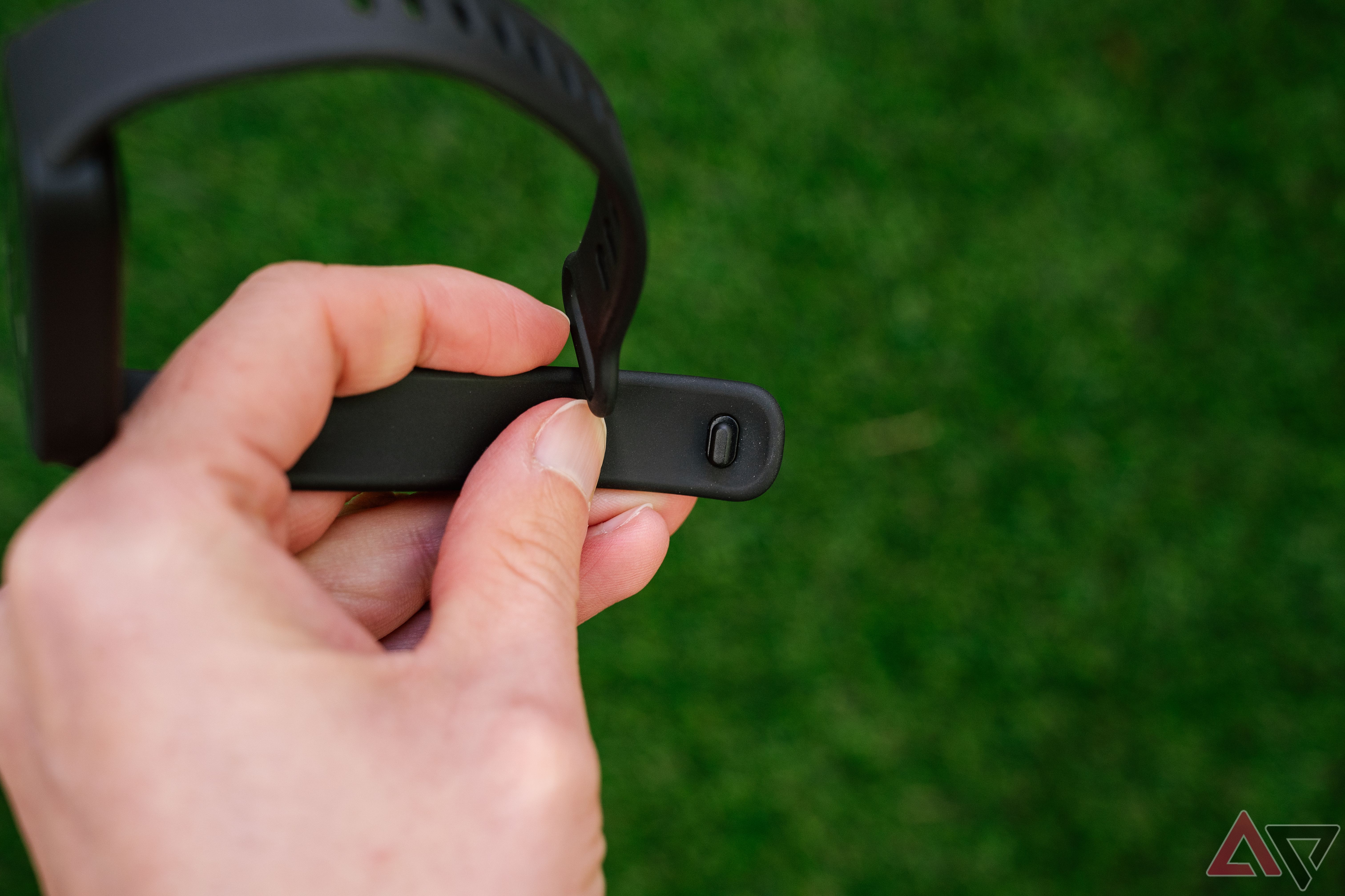 Uma mão segura a Xiaomi Smart Band 9 Active acima da relva verde desfocada.