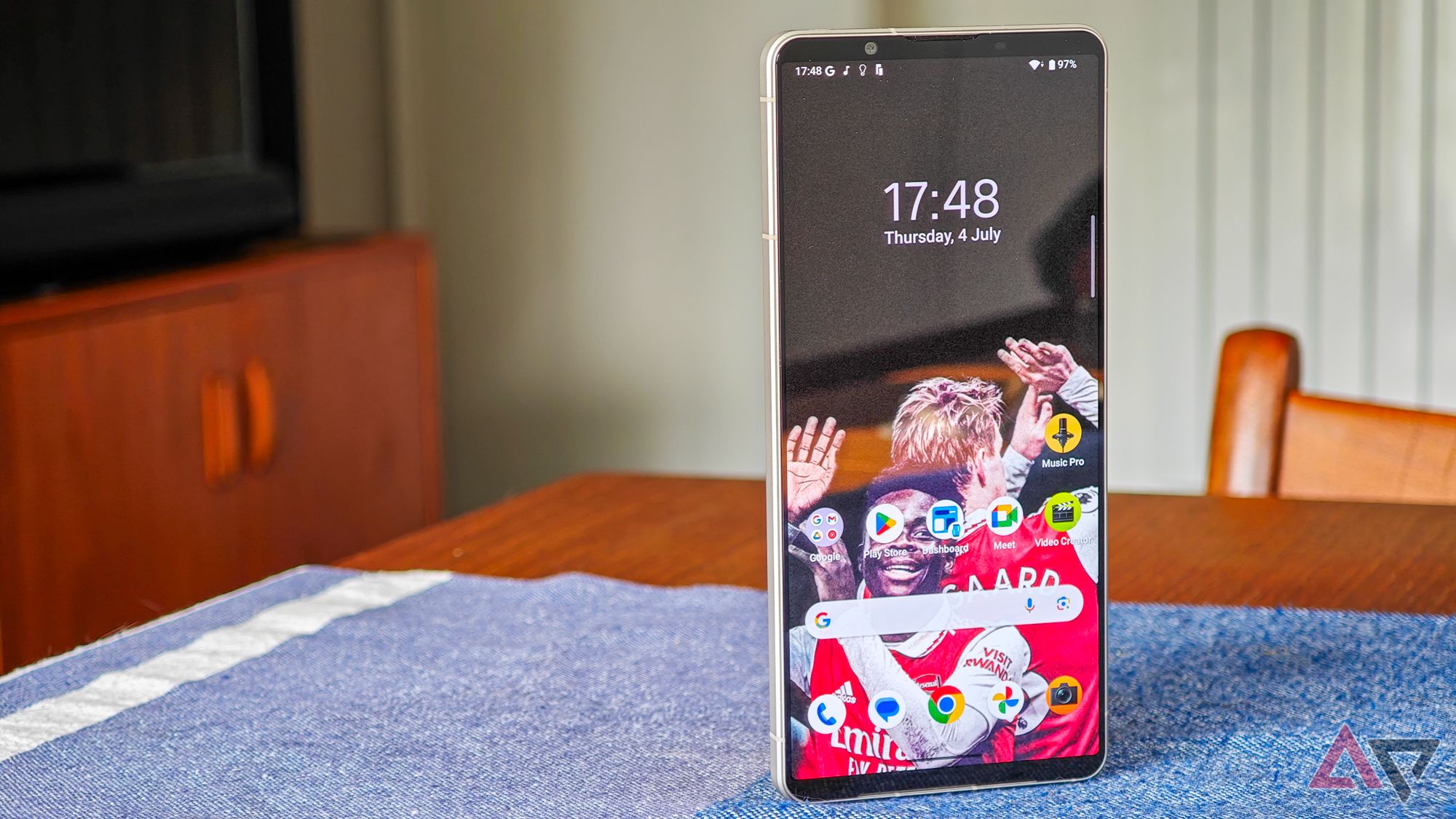 Uma foto do Sony Xperia 1 VI apoiado em uma mesa de madeira, mostrando a tela inicial com papel de parede do Arsenal