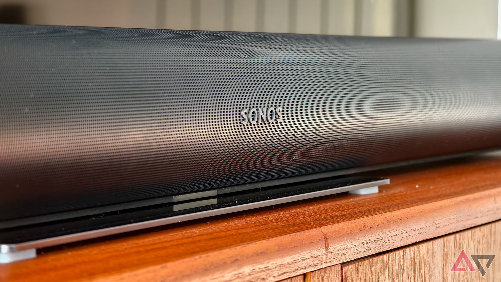 O logotipo da Sonos visível em uma barra de som Sonos Arc preta em um suporte de TV de teca