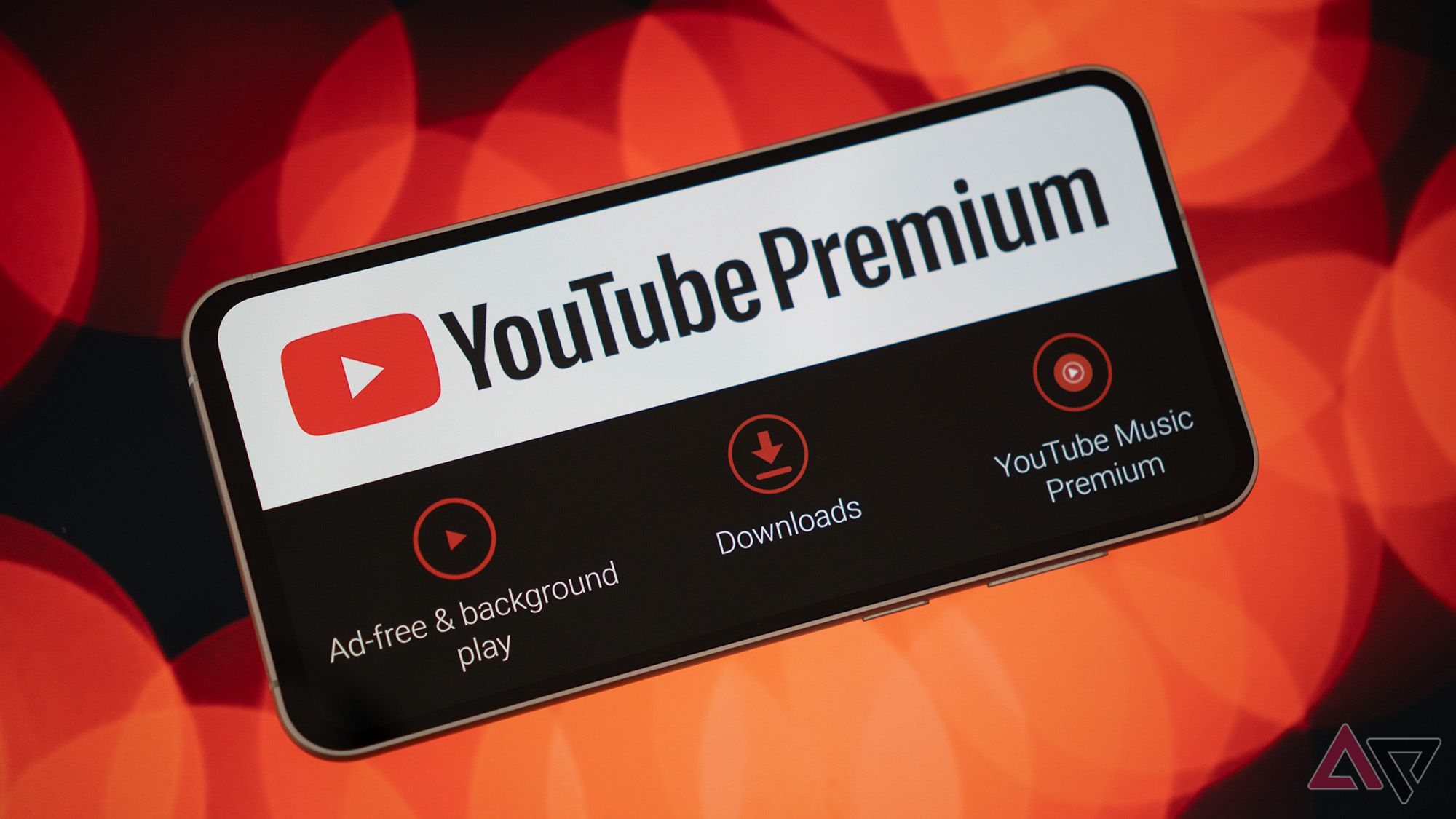 Um telefone exibindo o logotipo e recursos do YouTube Premium em um fundo bokeh vermelho.